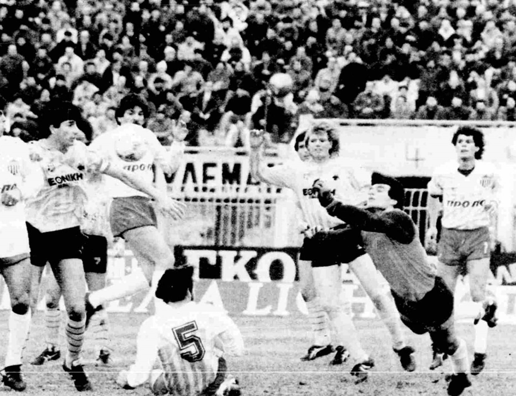 Στη λεζάντα ➢ Με γροθιές αποκρούει ο Δοξάκης μπροστά στην εστία του. Στο έδαφος βρίσκεται ο Παπαδόπουλος, ενώ καραδοκούν Μανωλάς και Νίλσεν.